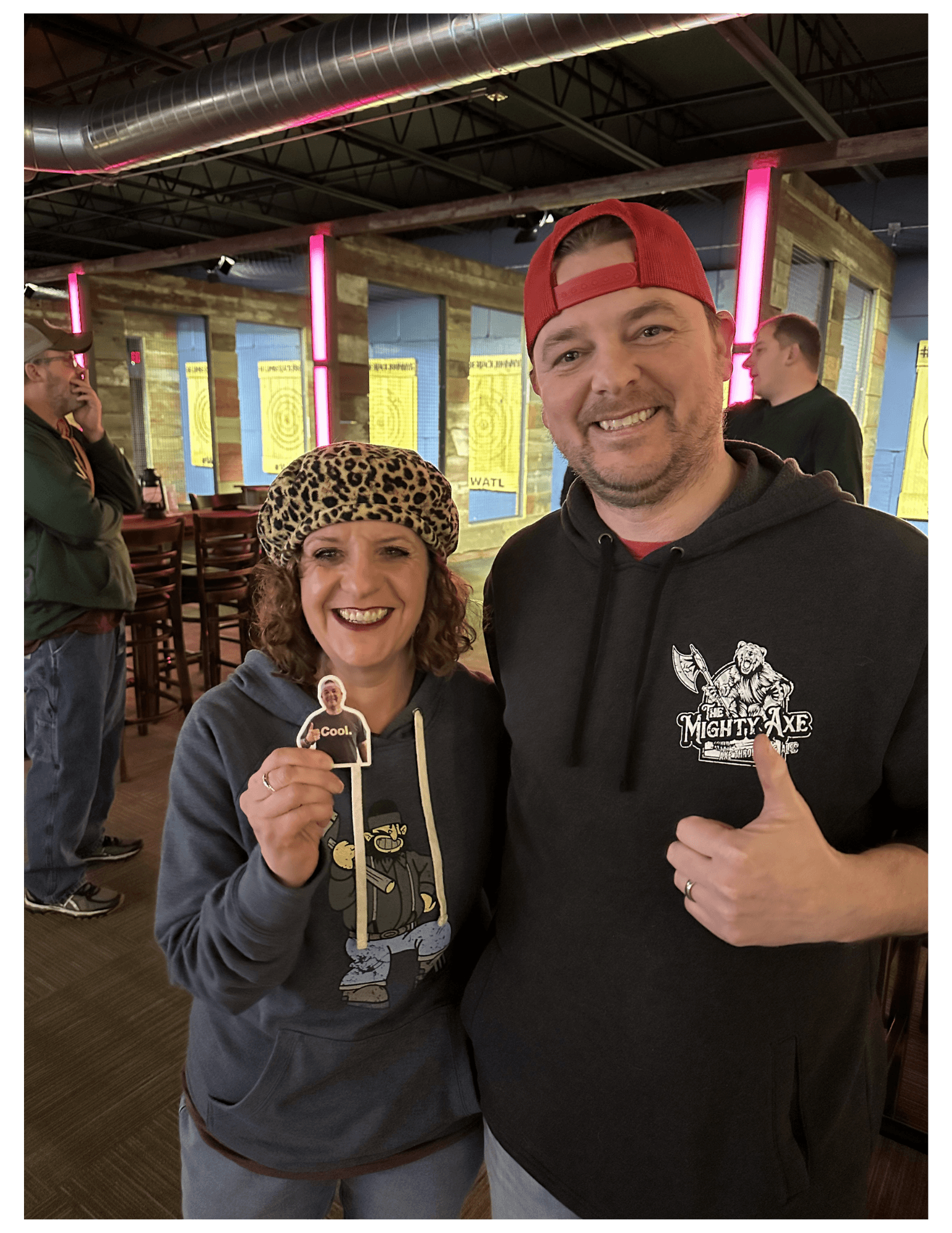 Smiling man and woman pose in an axe-throwing venue with targets in the background.