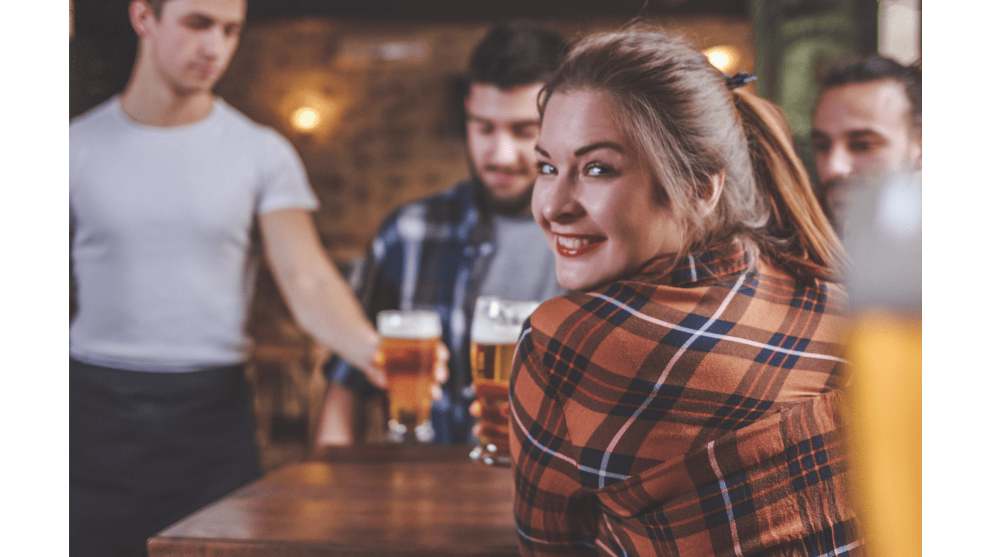 Smiling woman in a plaid shirt looks back while a waiter serves beer at a bar.