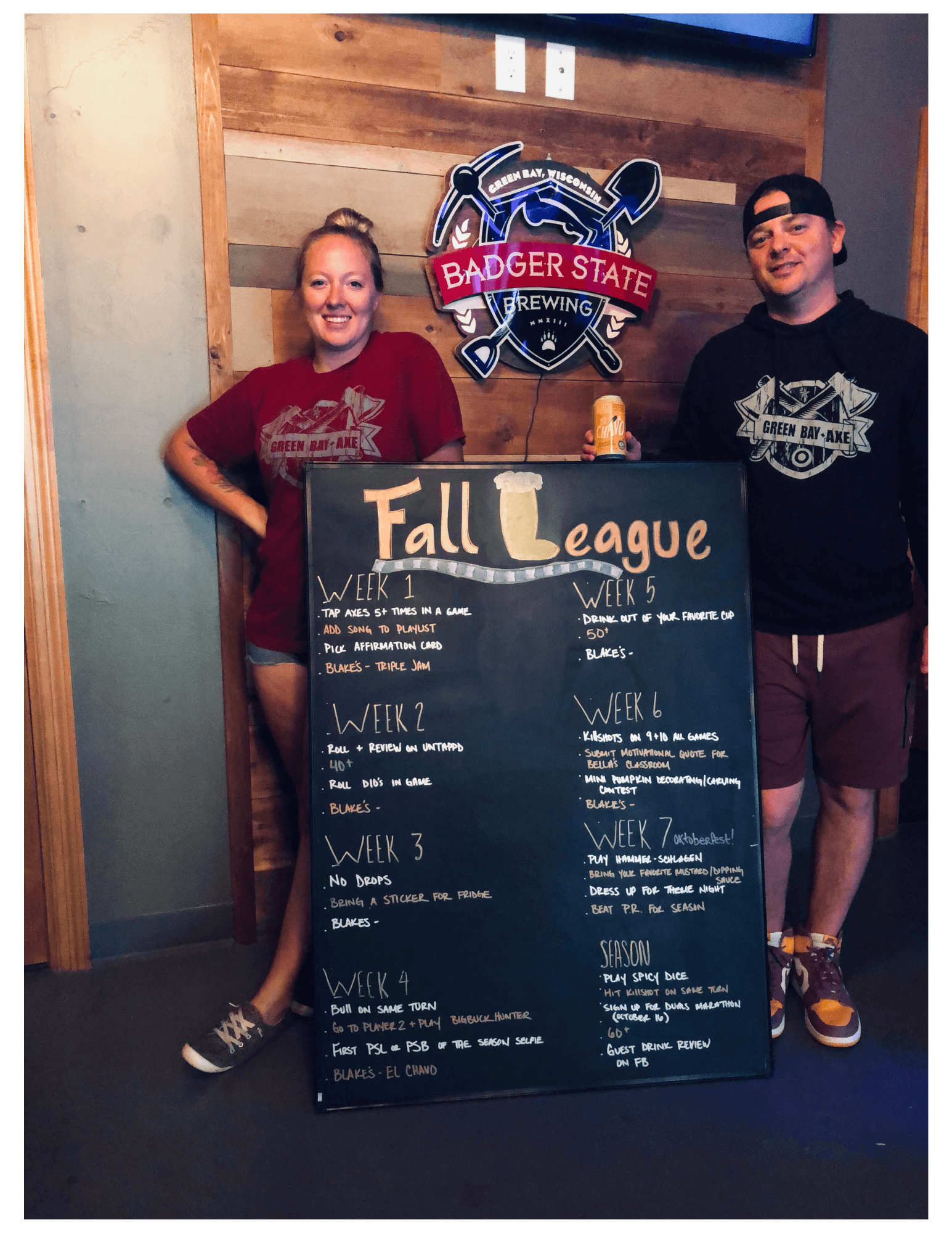 Two people pose with a Fall League schedule chalkboard at Badger State Brewing.
